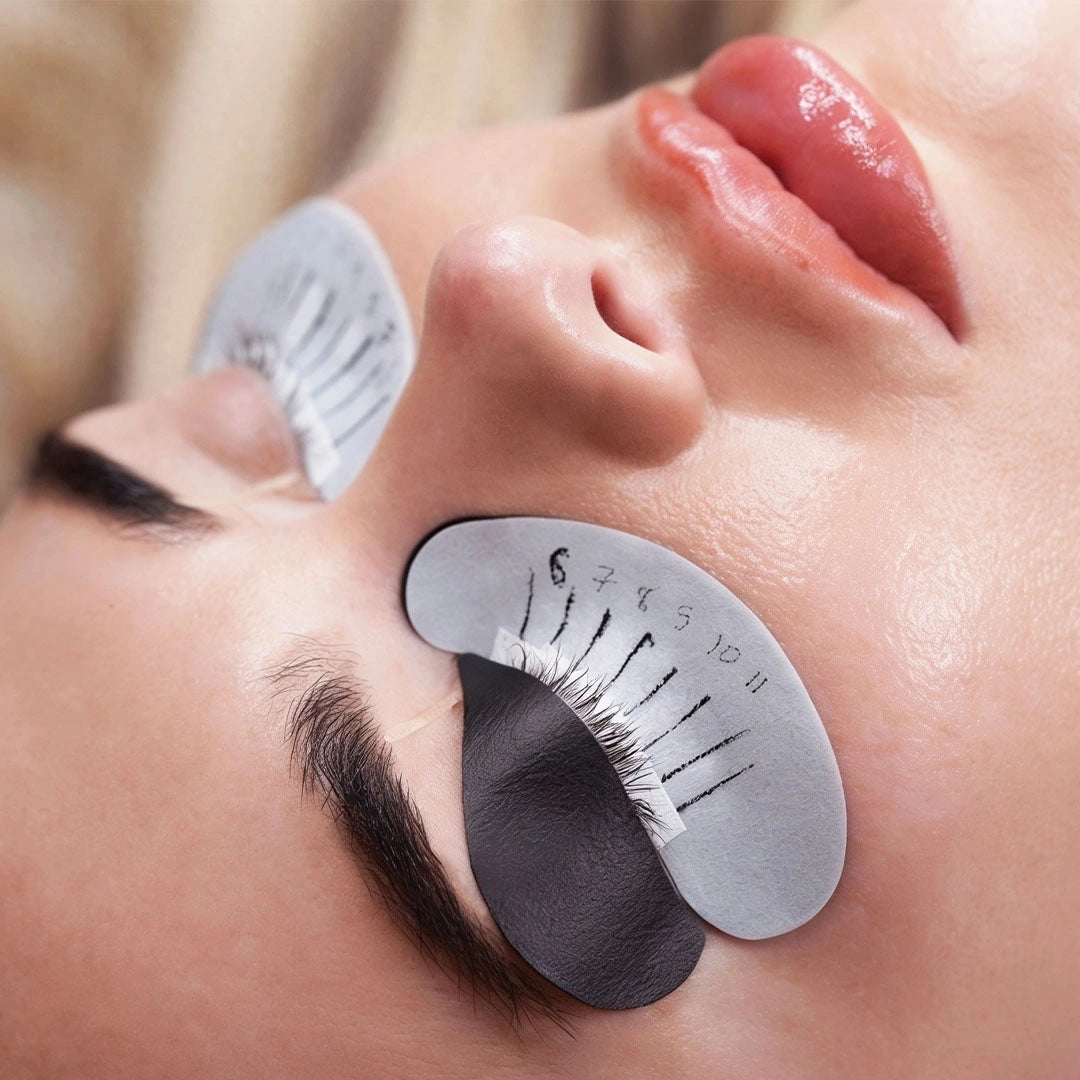Close-up of a client with black bio gel upper eye pads and white lash mapping under-eye pads applied during a lash extension treatment.
